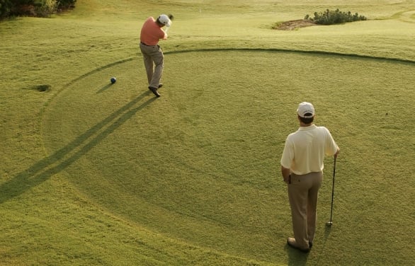 Two friends golfing in the Texas Hill Country. Player is in mid swing and friend is watching to see where his shot goes.