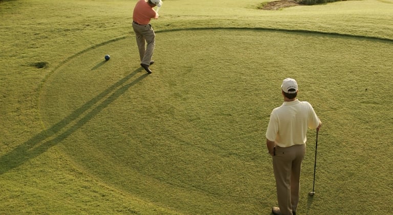 Two friends golfing in the Texas Hill Country. Player is in mid swing and friend is watching to see where his shot goes.