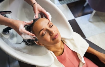 A woman in a pink shirt getting her hair washed by a professional at the spa.