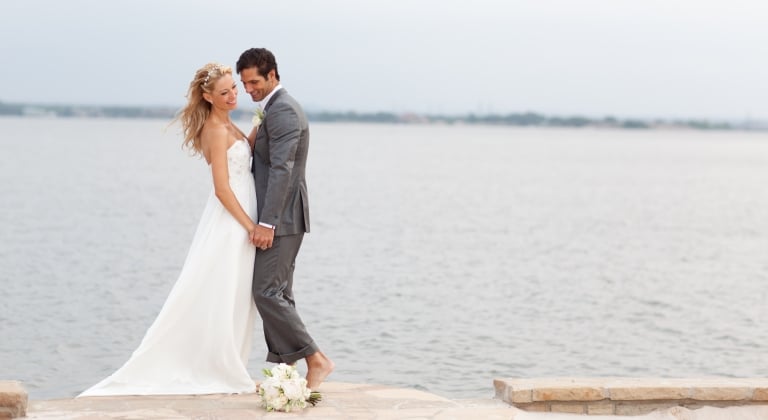 Newlyweds, bride and groom, standing lakeside and admiring the view.