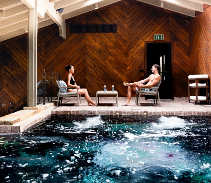 A man and a woman sitting next to the indoor swimming pool.