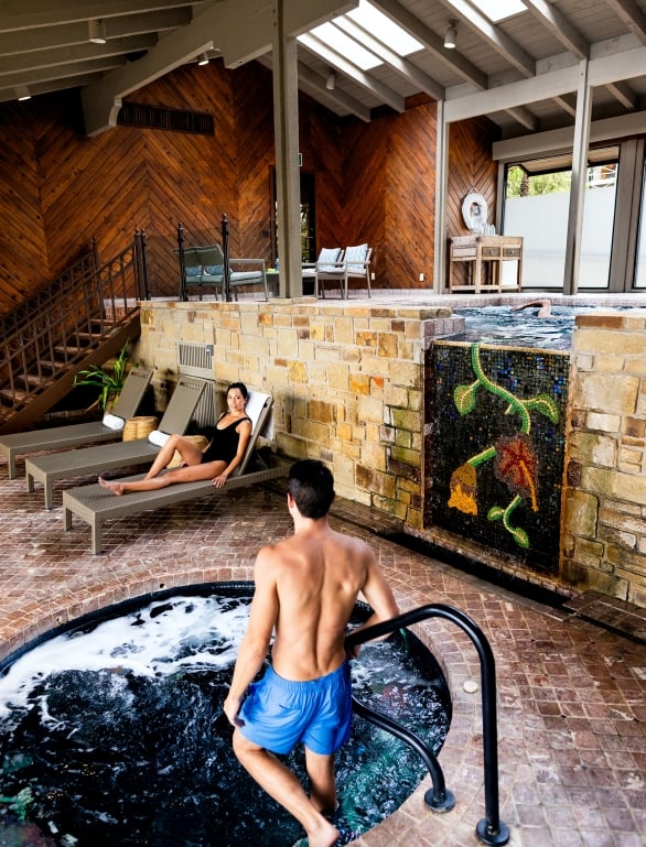 Man stepping down into the hot tub while looking at his friend sitting on a lounger
