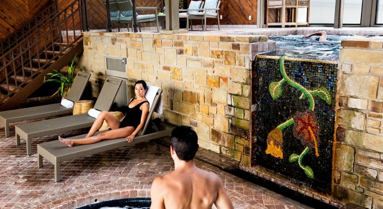 Man stepping down into the hot tub while looking at his friend sitting on a lounger
