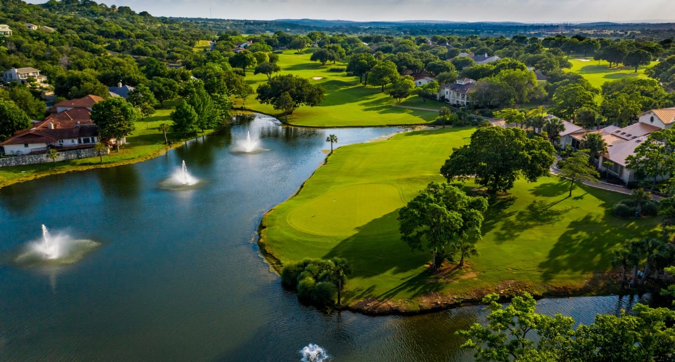 Large body of water with three fountains next to the green of a golf course.