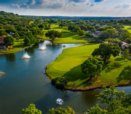 Large body of water with three fountains next to the green of a golf course.