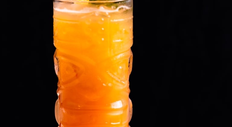 Signiture cocktail with a vibrant orange color and garnished with pinnaple.