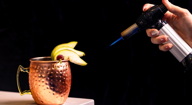 Moscow mule garnished with pear that is being torched to create flavor.