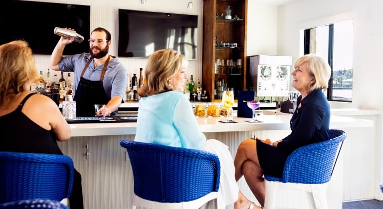 Two women sitting in blue bar stools having cocktails at the bar.