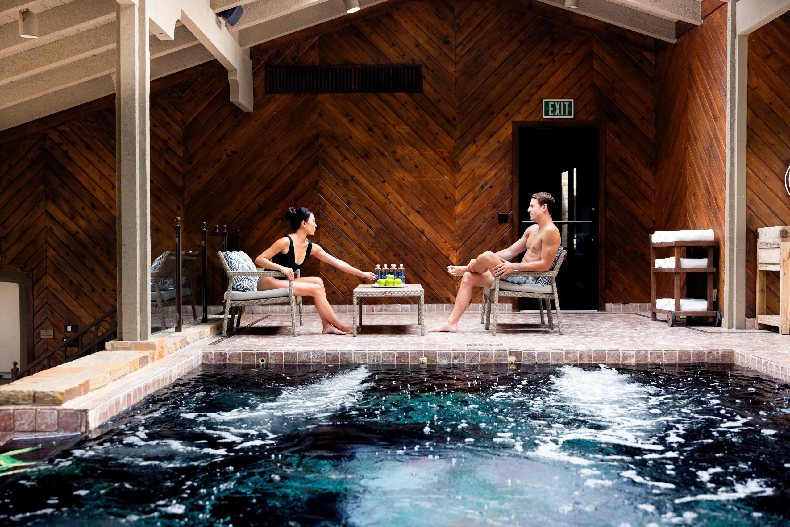 A man and a woman sitting by the indoor pool at the spa.