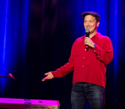 Rob Schneider with microphone in hand telling a joke.