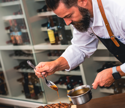 Chef glazing large steak in the kitchen.