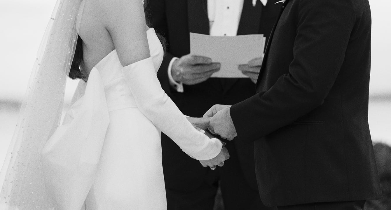 Wedding couple holding hands. Groom placing ring on brides hand as they say their