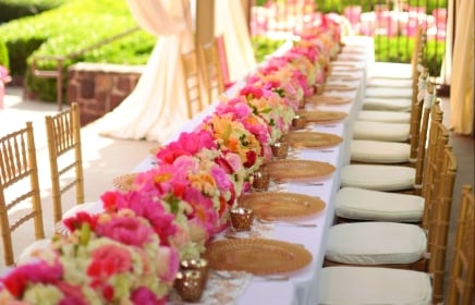 Pink and yellow flowers line the long table for the wedding party