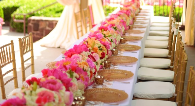 Pink and yellow flowers line the long table for the wedding party