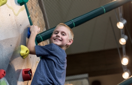 young boy looking down at the camera while climbing the rock wall in the jungle kids club